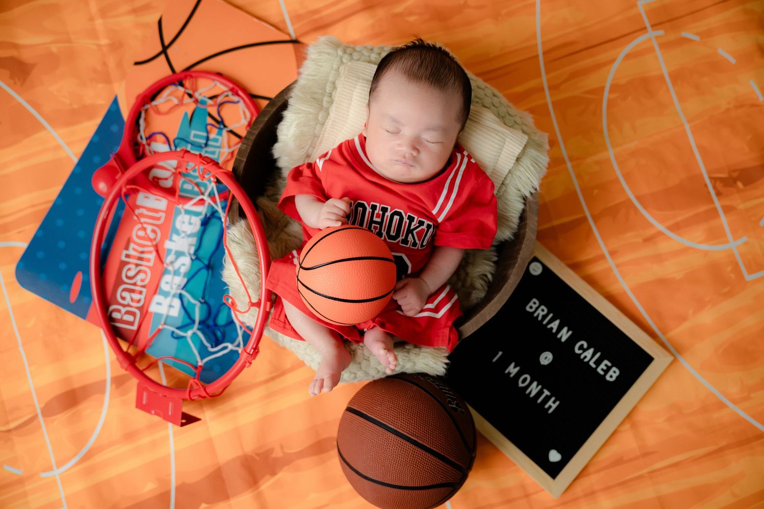 Basketball themed milestone photo session with orange court backdrop and sports equipment.