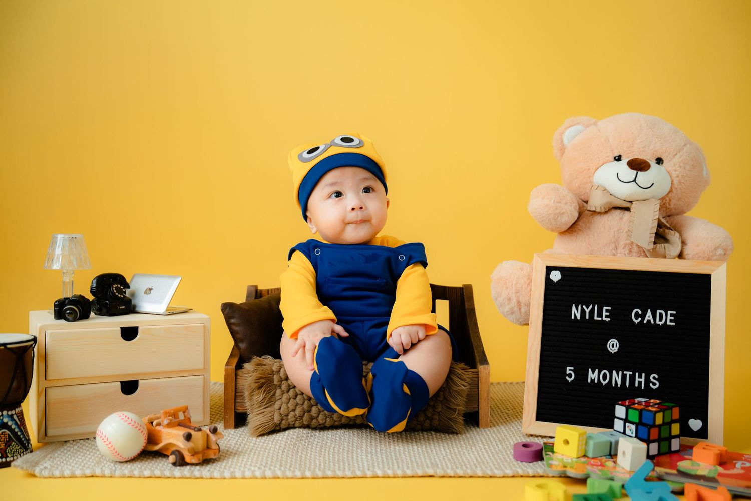 Yellow backdrop photoshoot with toy blocks, teddy bear and black letterboard.