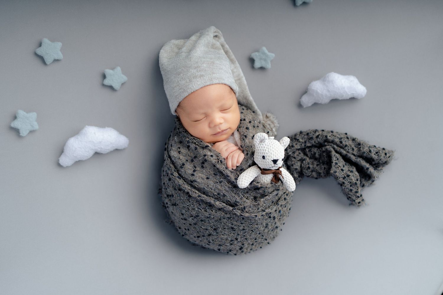 Newborn photography setup with gray cushions, white stars and cloud decorations in a dreamy celestial theme.