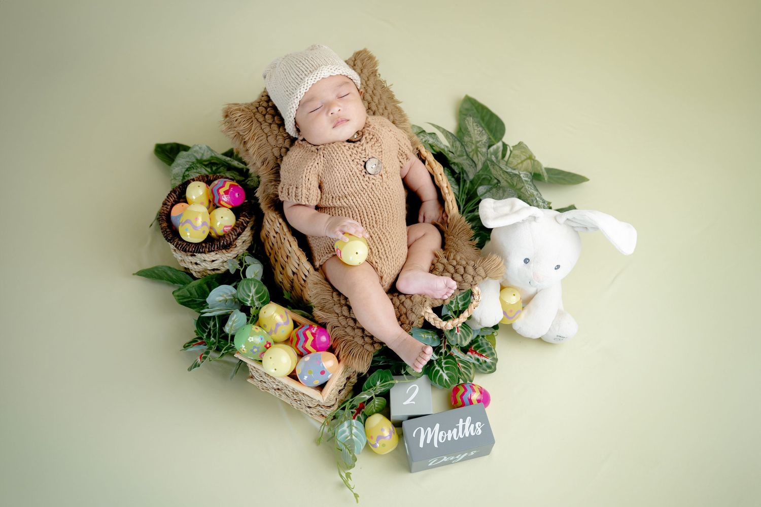 Easter themed photo setup with bunny, eggs, and floral decorations on soft green background.
