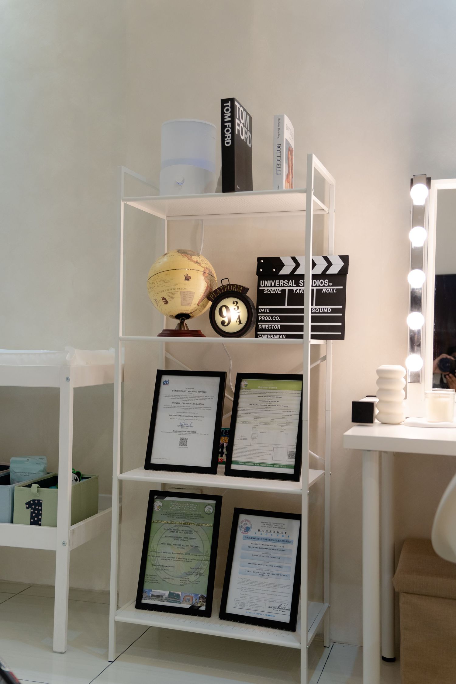 White shelving unit displaying certificates, movie props, and decor items in a studio setting.