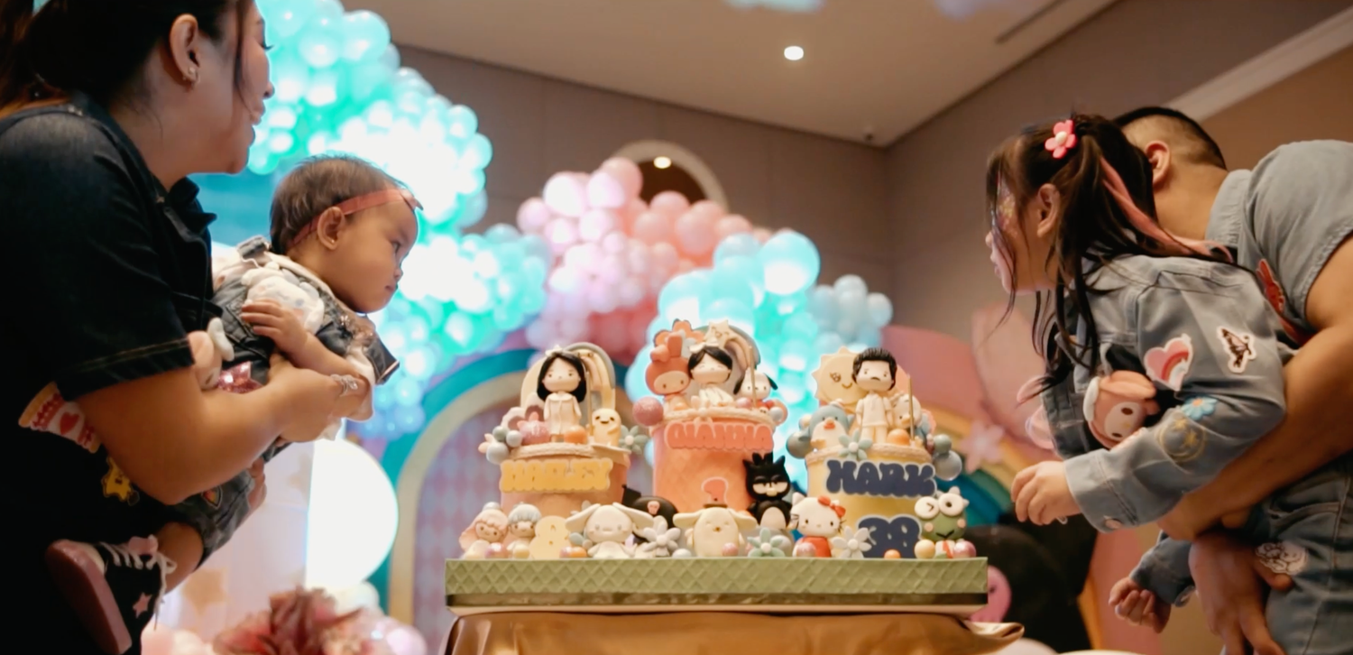 A colorful birthday party setup with a decorated cake, balloon arch, and children gathered around a festive table.