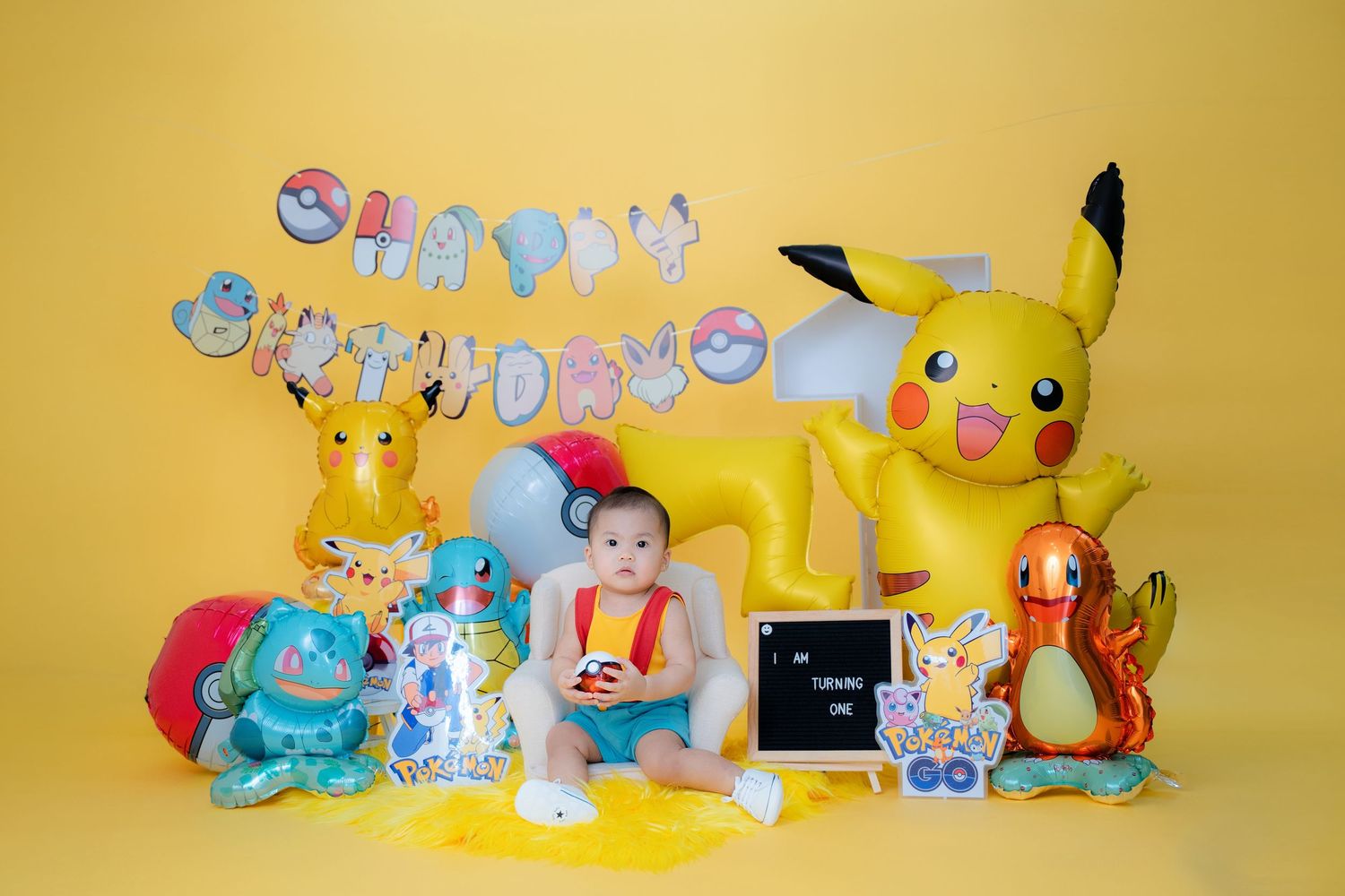 Pokemon themed photo setup with plush toys and decorations against yellow backdrop.