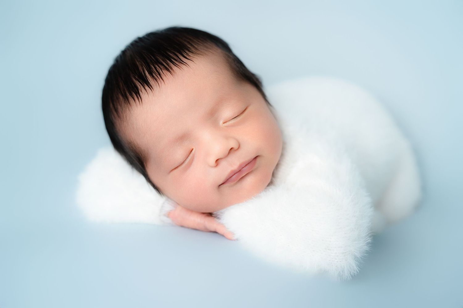 Peaceful newborn resting with white stuffed toy on blue backdrop.