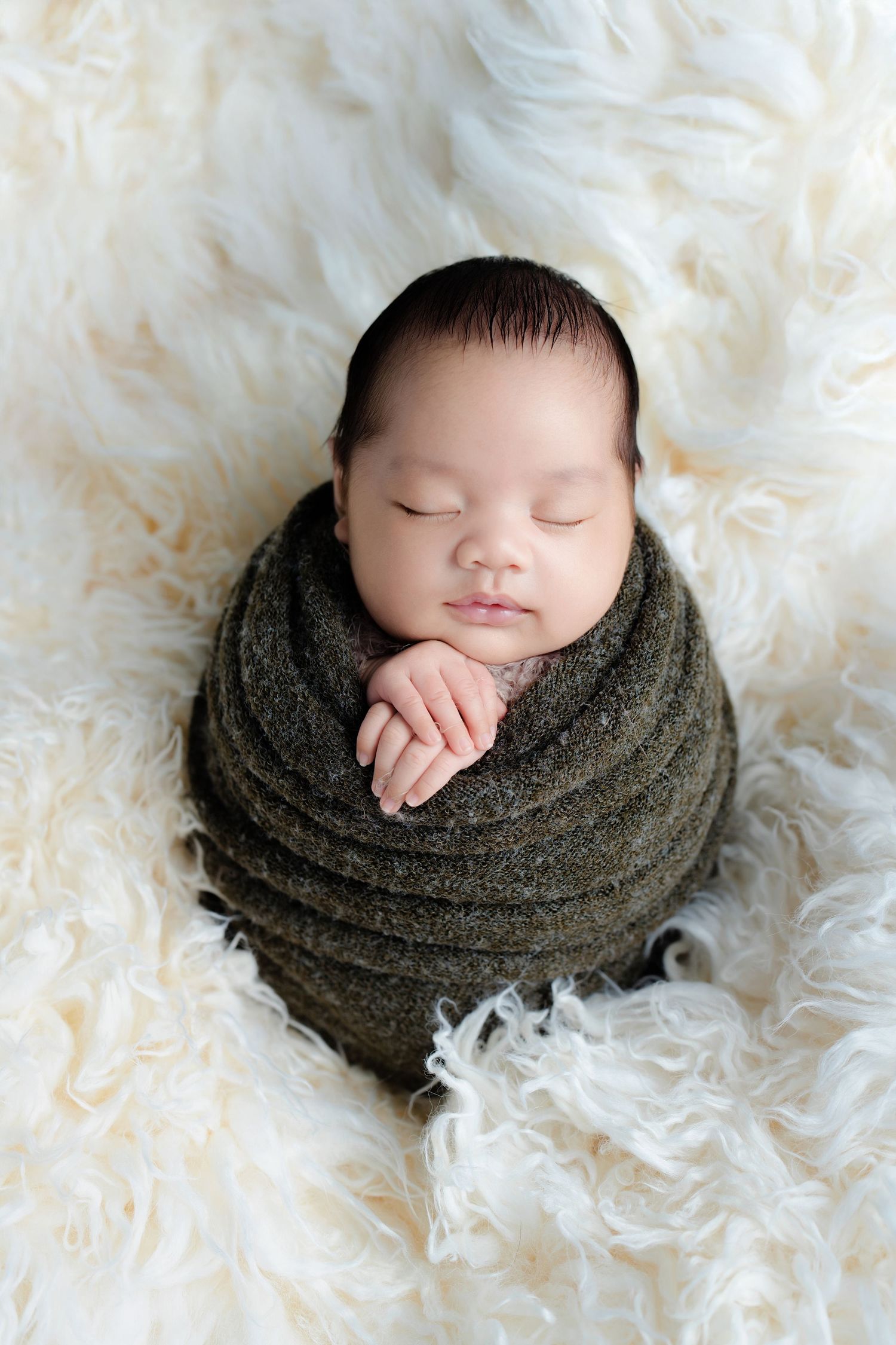 Sleeping newborn baby wrapped in dark gray knit wrap on white fluffy blanket shown in four sequential poses.