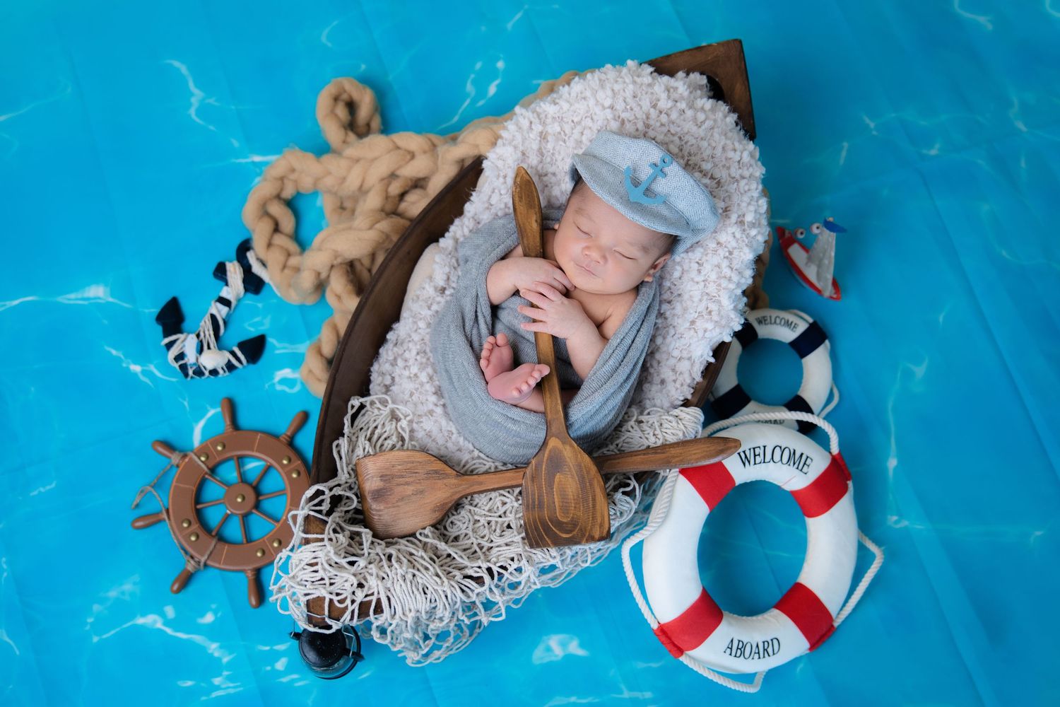 Maritime themed newborn photo setting with sailor accessories, life ring, and steering wheel on blue backdrop.