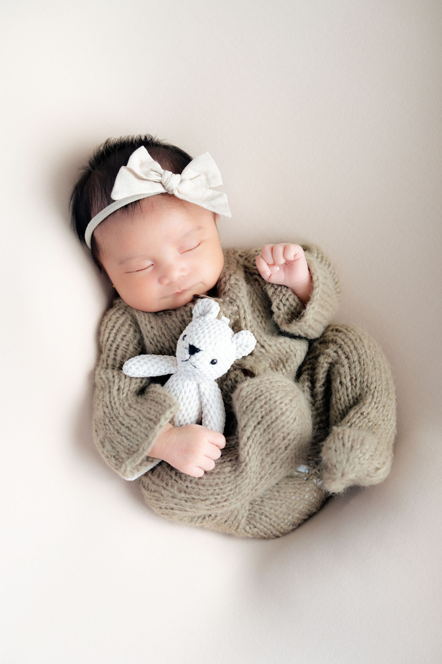 Newborn baby in gray knit wrap wearing white bow headband lying on white backdrop in three similar poses.