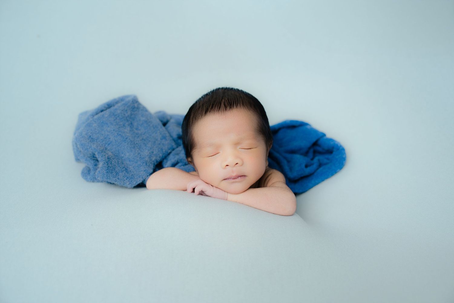 Newborn wrapped in a soft blue blanket on light blue background during photography session.