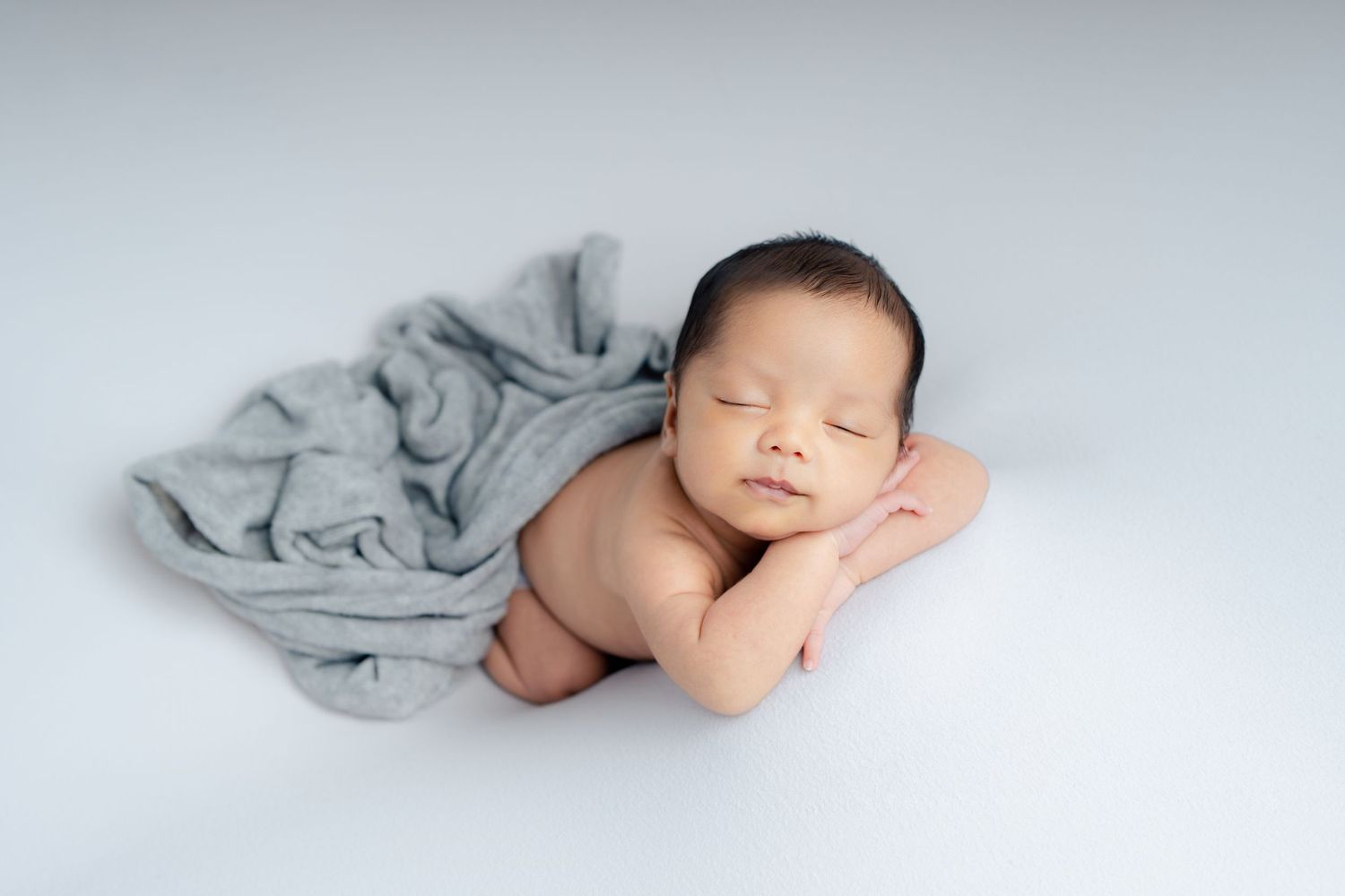 Peaceful sleeping newborn baby wrapped in soft gray blanket on white background.