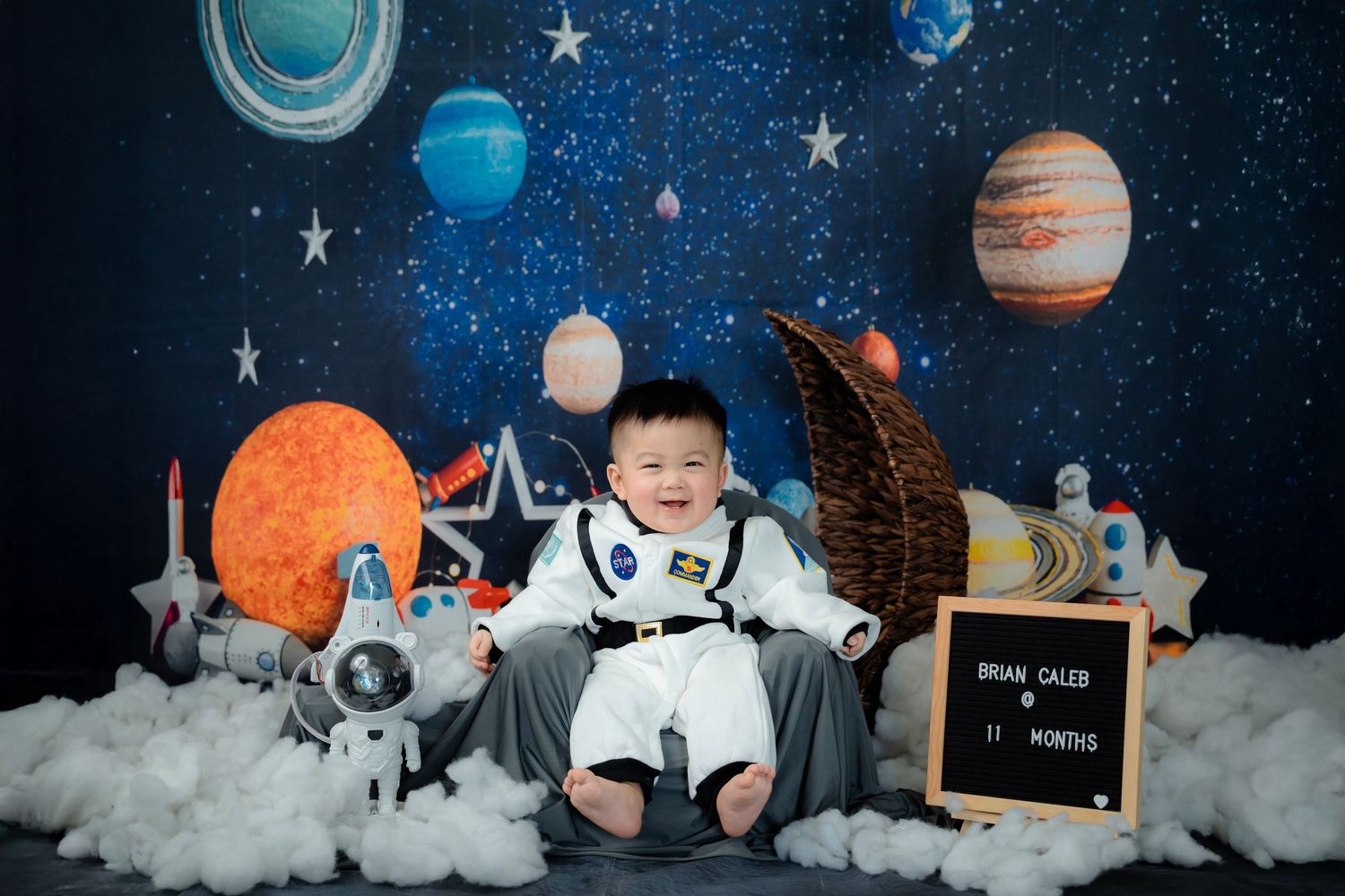 Space themed photo setup with planets, stars, and astronaut props against dark backdrop.