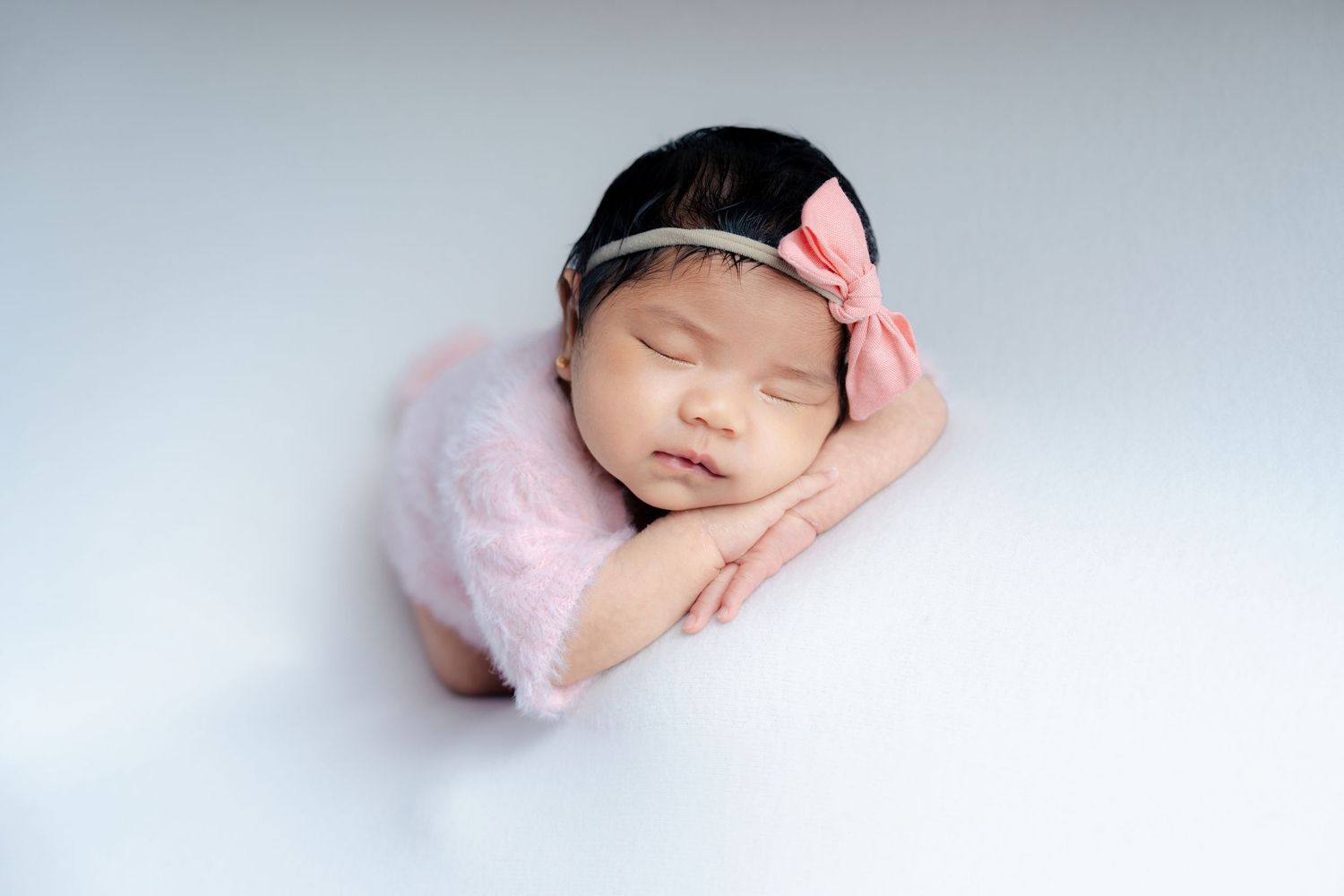 A sleeping newborn in soft pink wraps rests peacefully against a light background in a series of artistic poses.