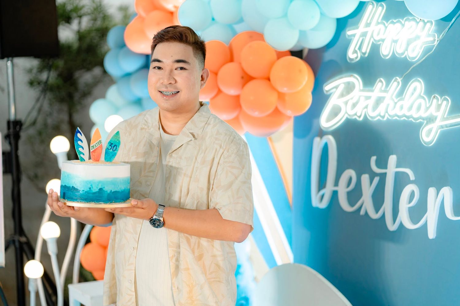 Man holding blue birthday cake at Dexter's birthday party with balloon arch backdrop.