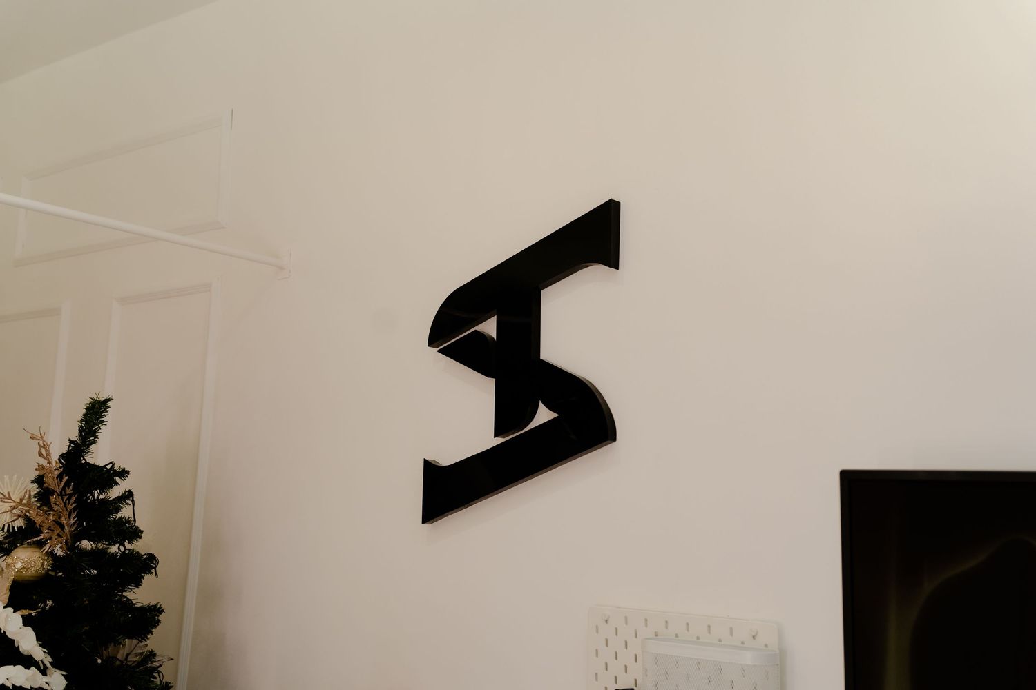 Black stylized 'S' logo mounted on a white wall as minimal modern decor.