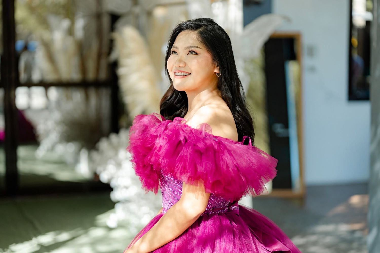 Woman in a vibrant fuchsia off-shoulder tulle gown smiling outdoors at an elegant venue.