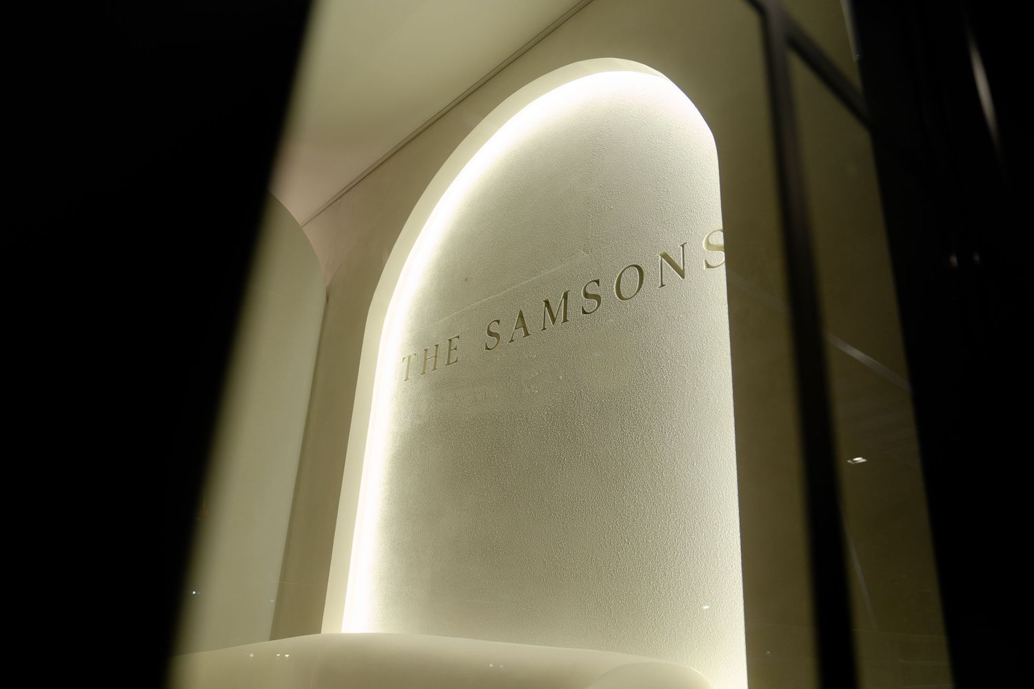 Dramatically lit curved archway displaying 'THE SAMSONS' text with ambient lighting creating a soft glow.