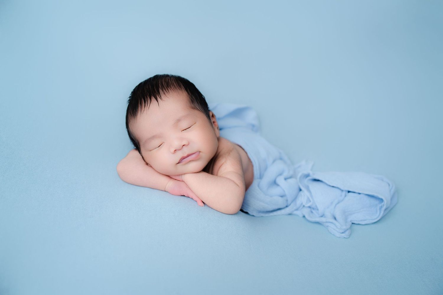 Newborn swaddled in light blue fabric against matching backdrop.