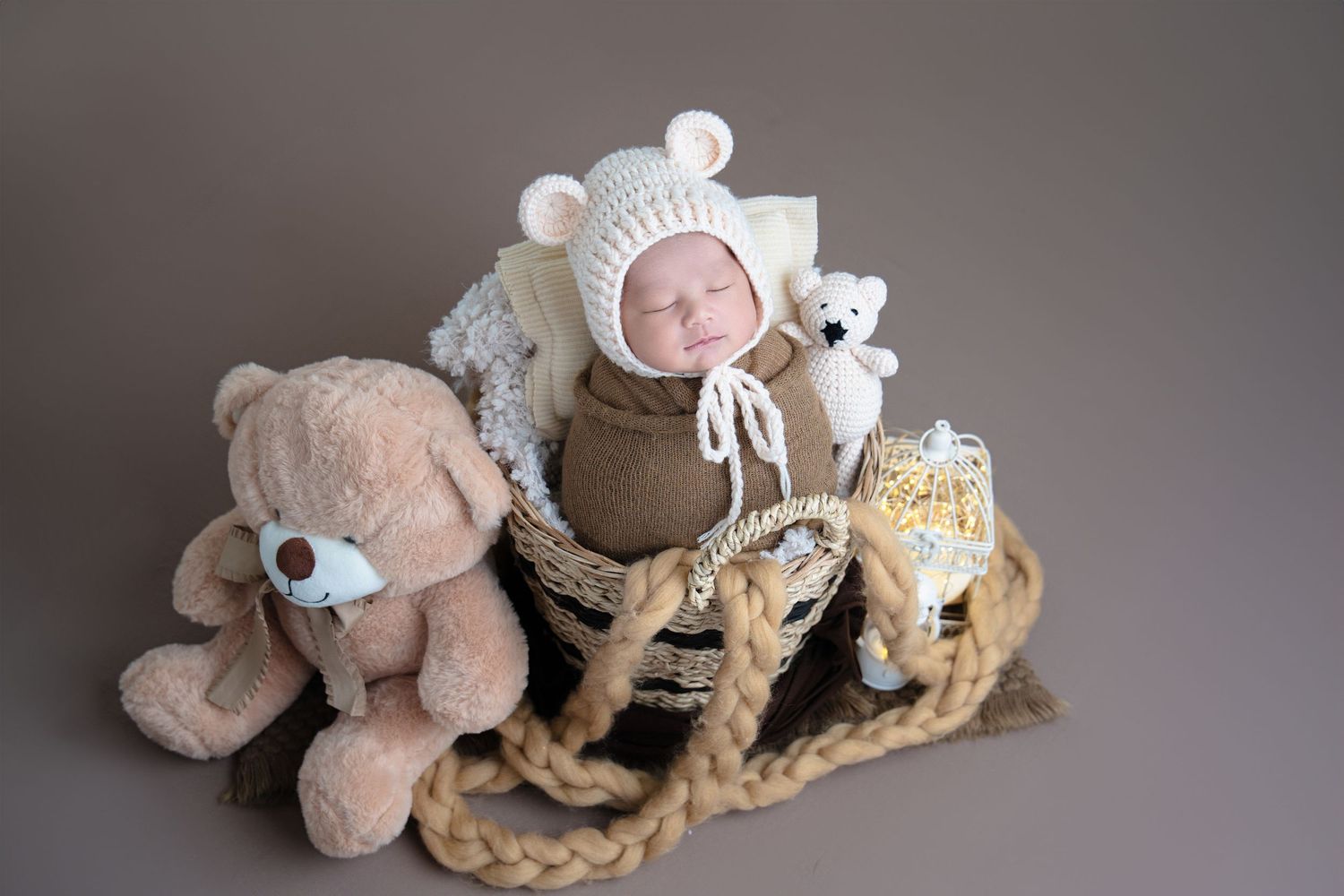 Cozy newborn portrait with knit bear bonnet surrounded by plush toys on neutral background.