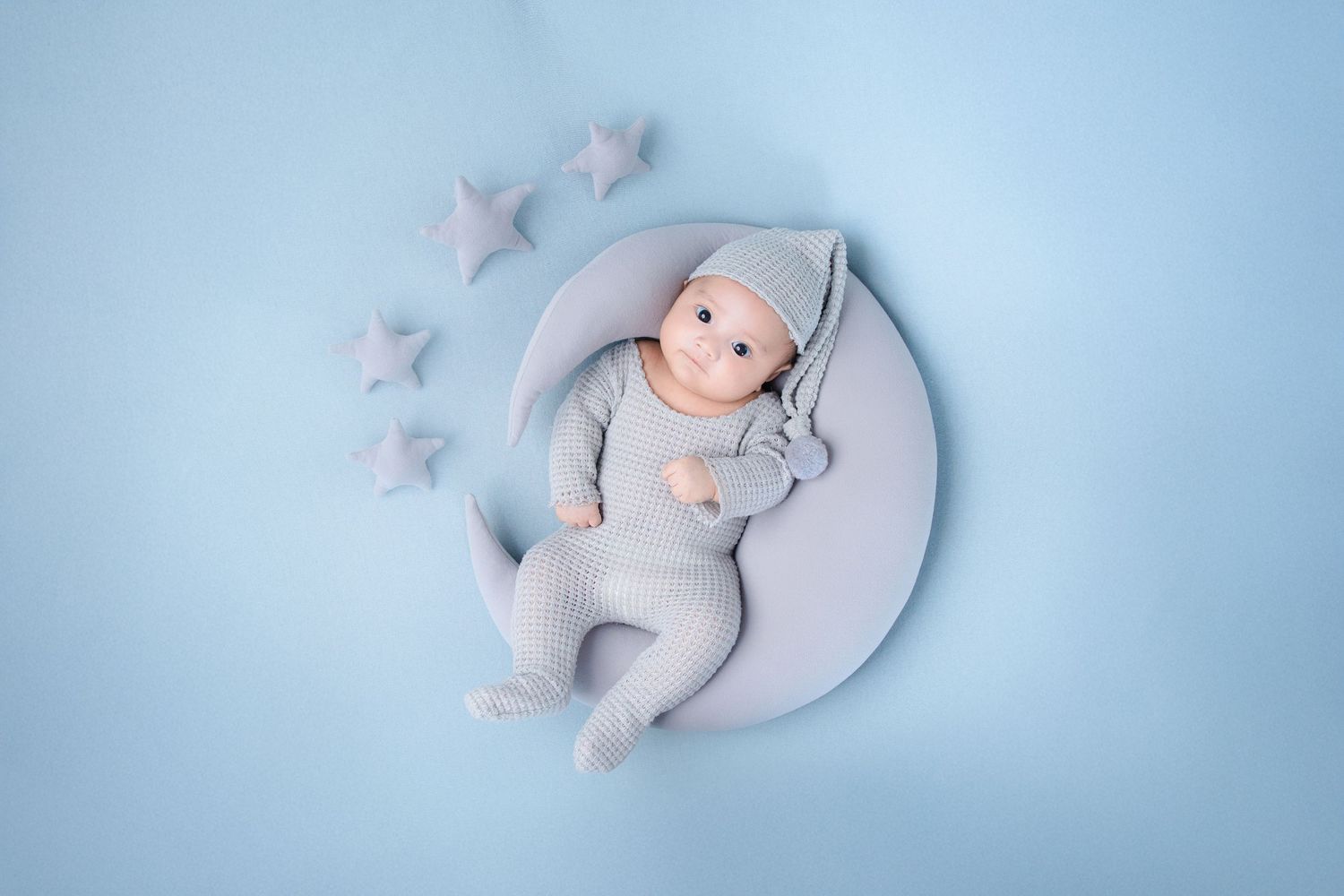 Sleeping newborn photographed on pale blue background with small white star decorations.