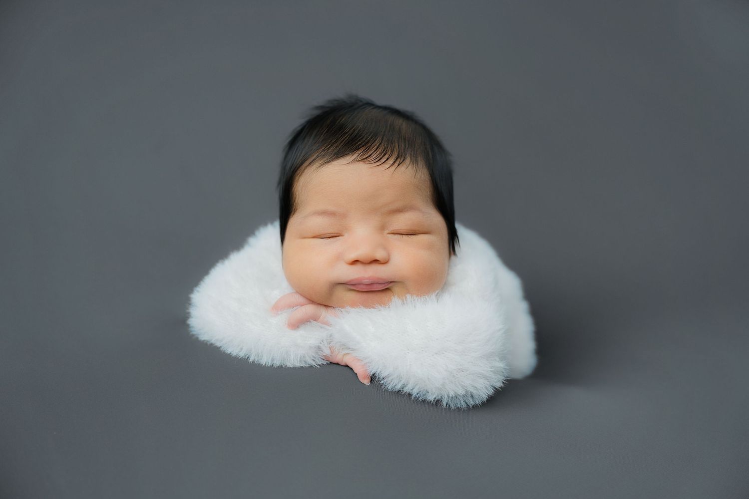 Peaceful newborn resting on white furry blanket in dark studio setting.