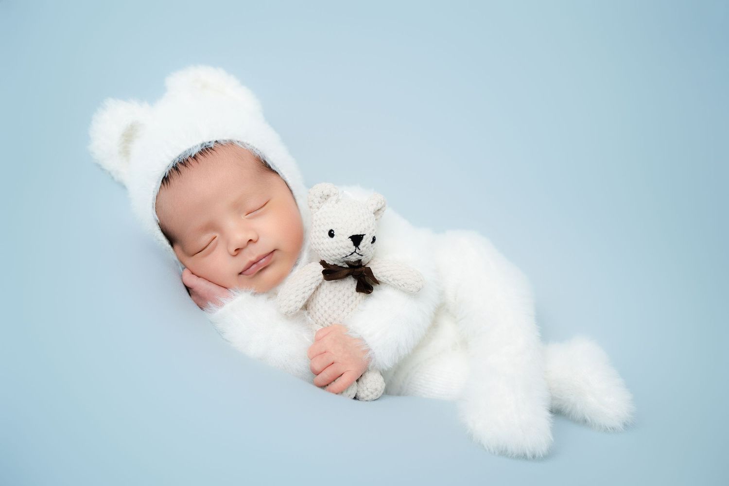 Sleeping baby cuddled with white plush polar bear on blue background.