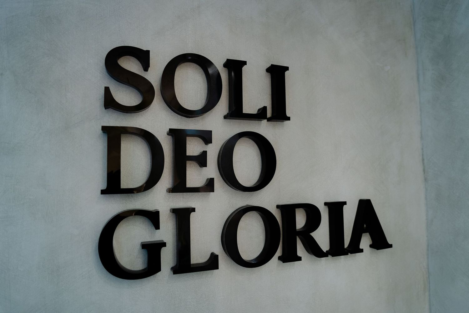 Black text reading 'SOLI DEO GLORIA' mounted on a light gray wall in bold letters.