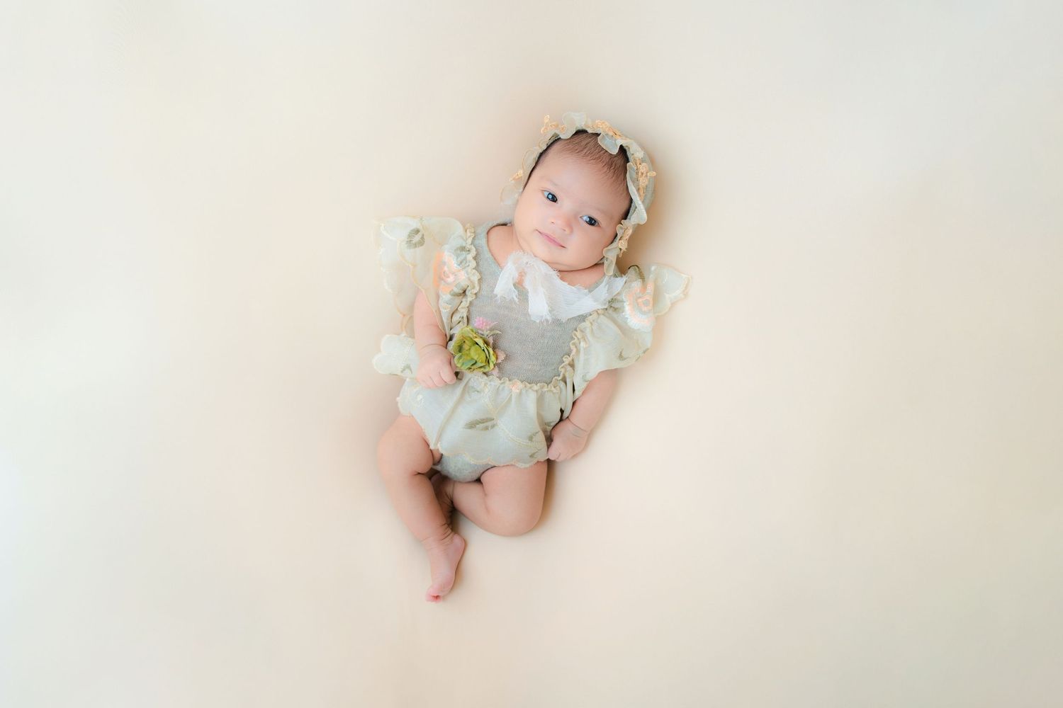 Newborn in mint green outfit lying on cream background with floral headband.