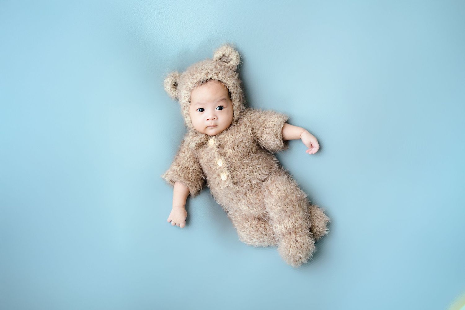 Sleeping newborn with plush teddy bear on light blue backdrop.