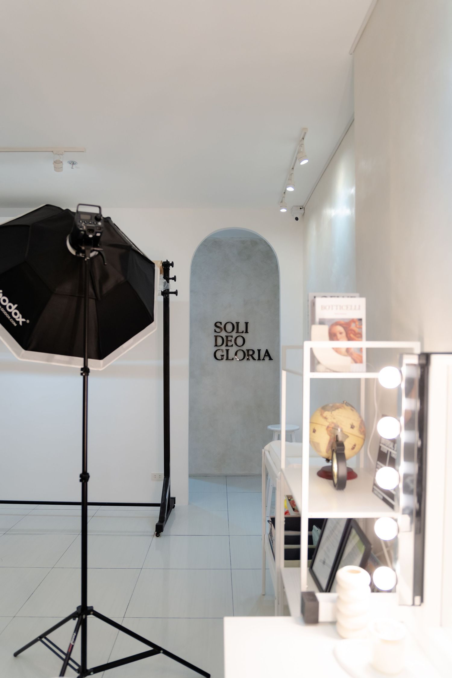Professional photo studio with lighting equipment and 'SOLI DEO GLORIA' text visible in an arched alcove.