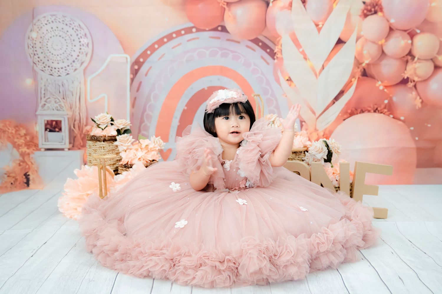 Baby photoshoot setup with pink tulle decorations, balloons, and soft plush toys in a dreamy nursery setting.