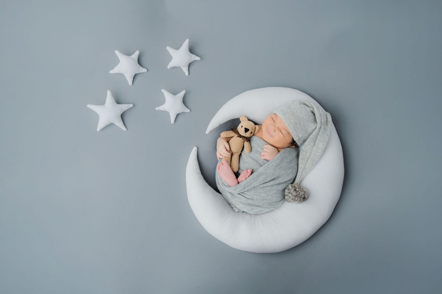 Newborn sleeping peacefully on crescent moon prop with white stars against blue backdrop.