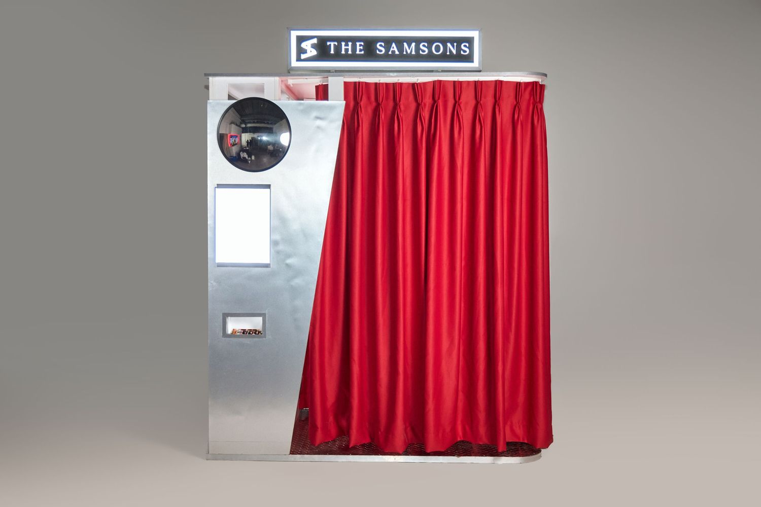 The Samsons photo booth with red curtain and silver exterior on gray background.