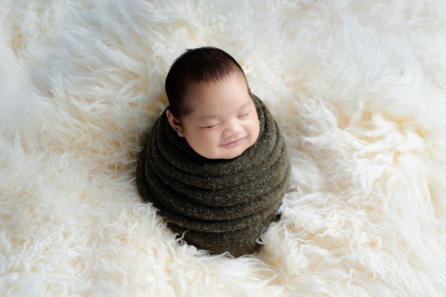 Newborn baby sleeping peacefully on soft white fluffy blanket in artistic black and white photography series.