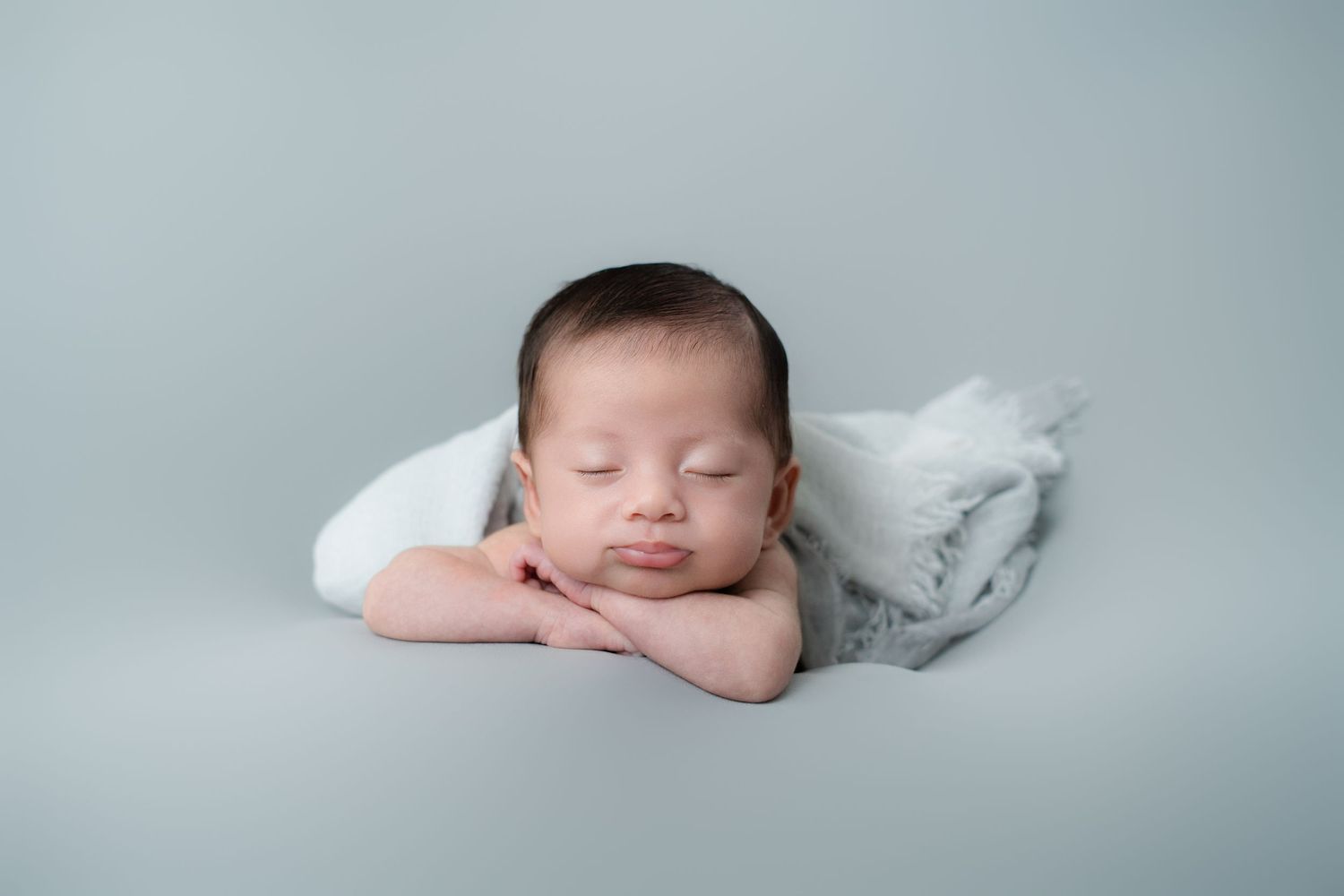 Peaceful newborn baby resting on white cushion during professional photo session.