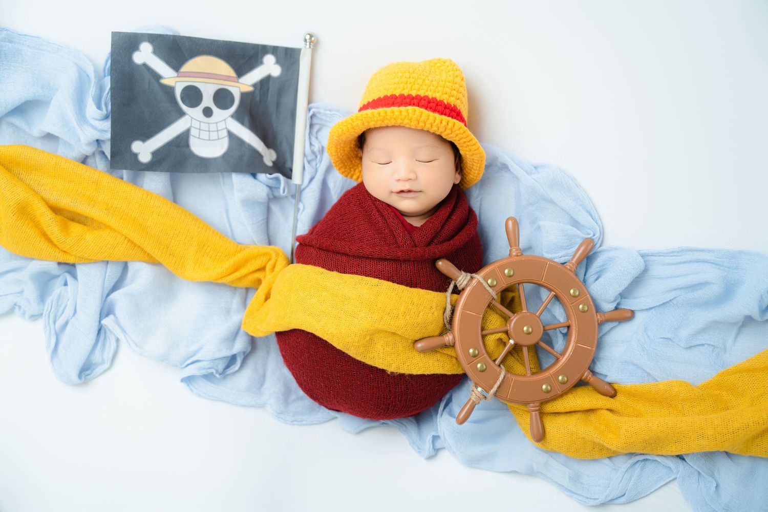 Nautical theme newborn photo with pirate flag and ship wheel props.