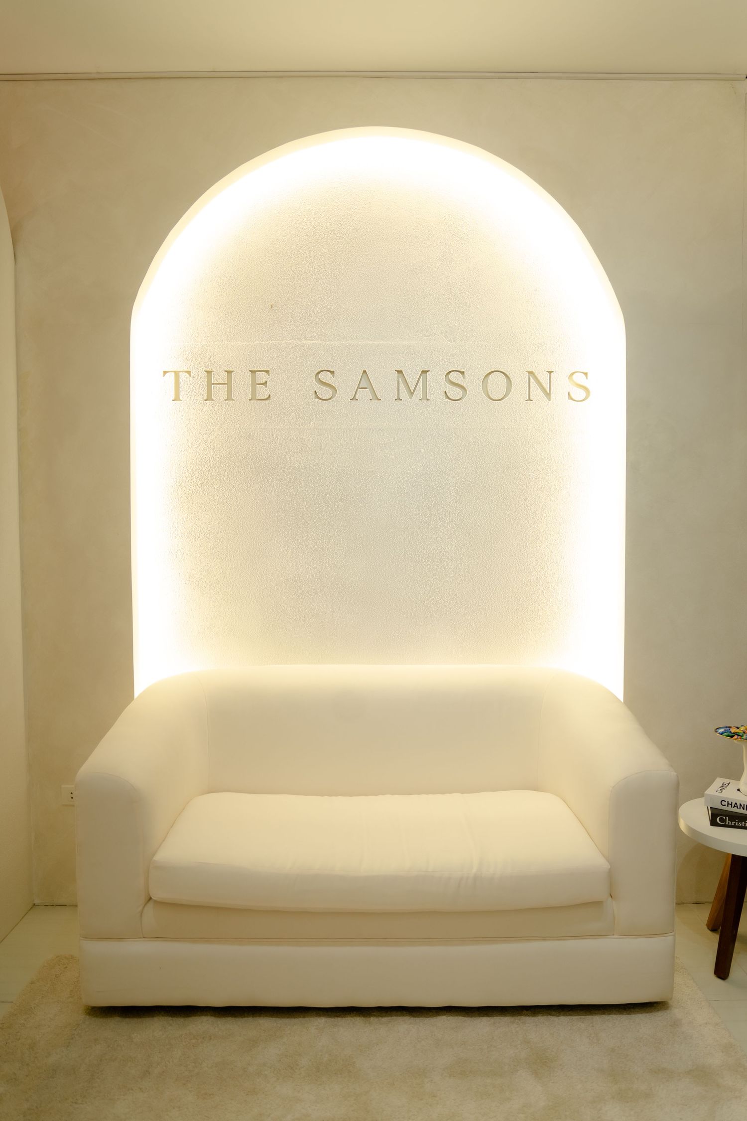Illuminated white archway nook with 'THE SAMSONS' text and white bench seating creating an elegant entryway display.