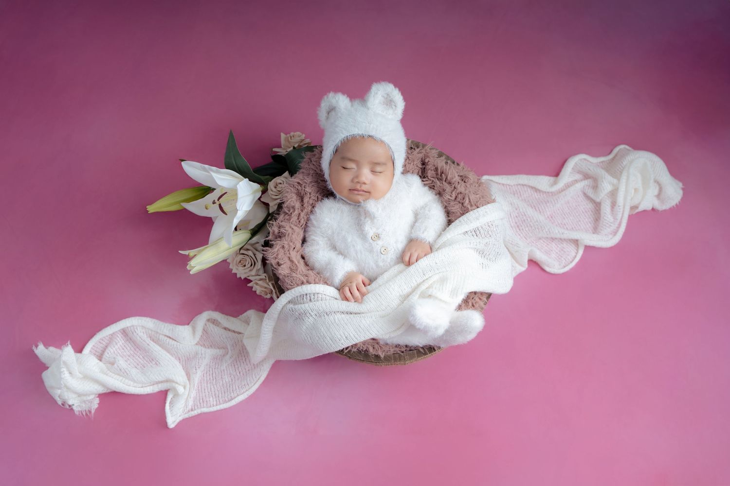 A baby wearing white clothing lies on a pink background in a series of connected artistic newborn portraits.