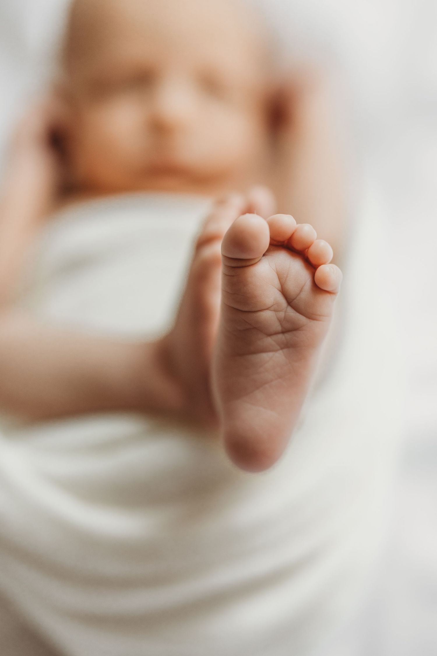 Close-up of a newborn baby's tiny foot with delicate toes, wrapped in a soft white blanket.
