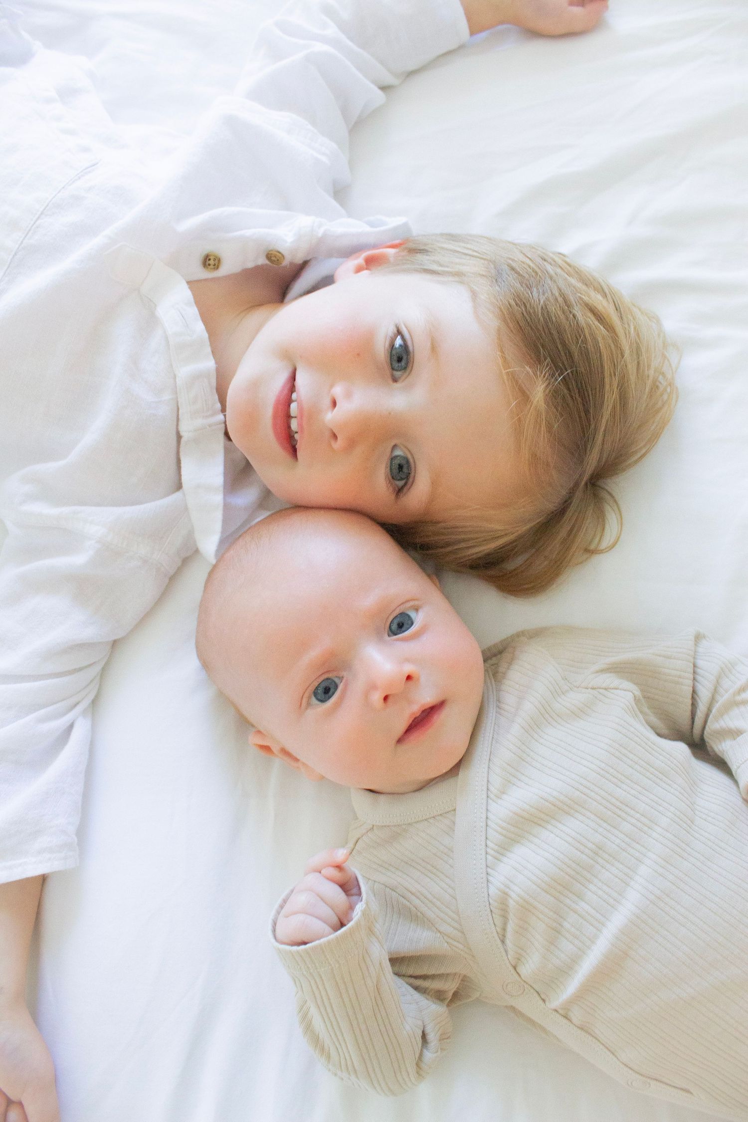Big brother and a newborn baby sibling laying on a bed during a family photography session in Fairfield County, CT.