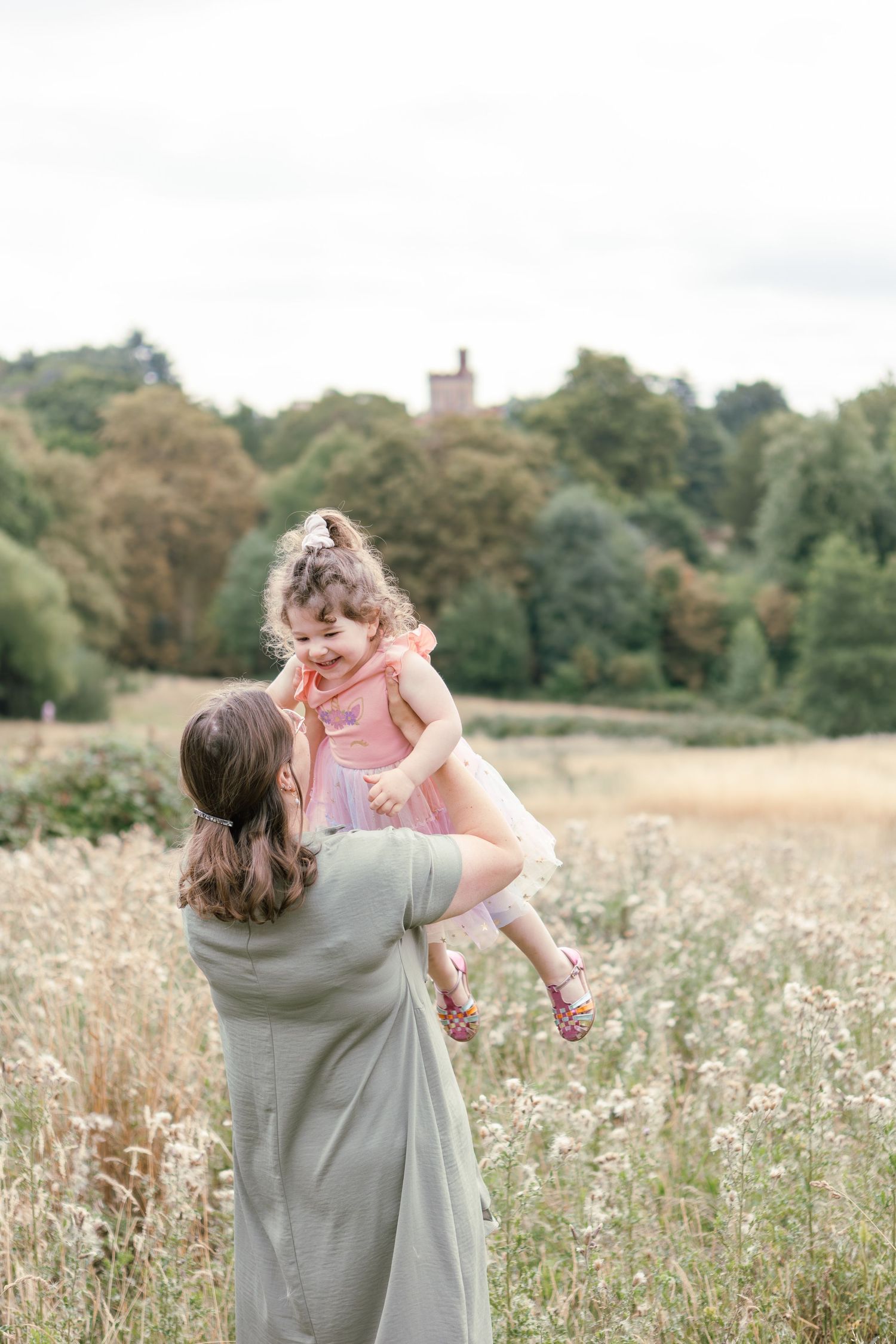 Mother lifts toddler girl into the air in outdoor meadow, girl smiles
