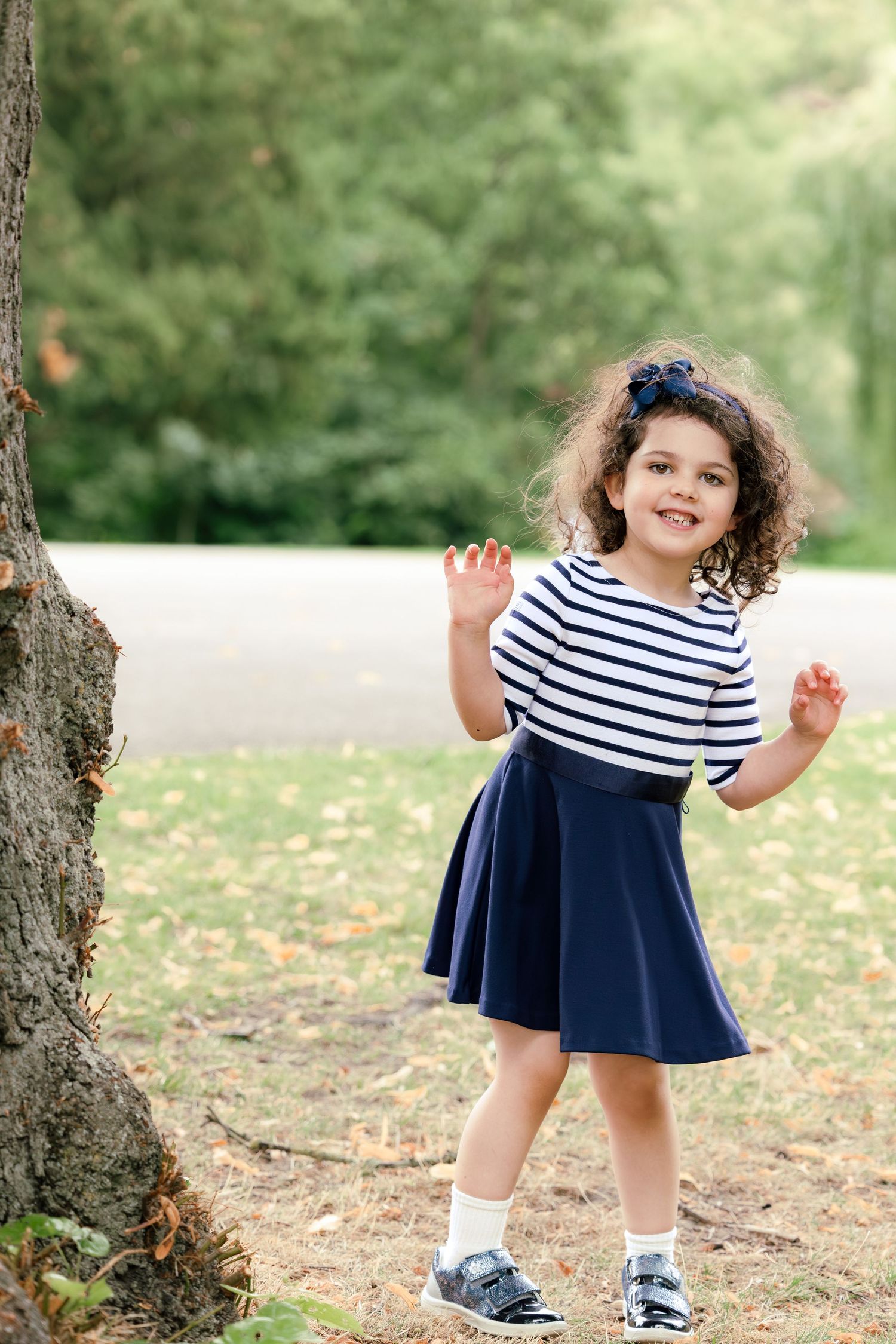 Girl playing peek a boo in park beside a tree and smiling
