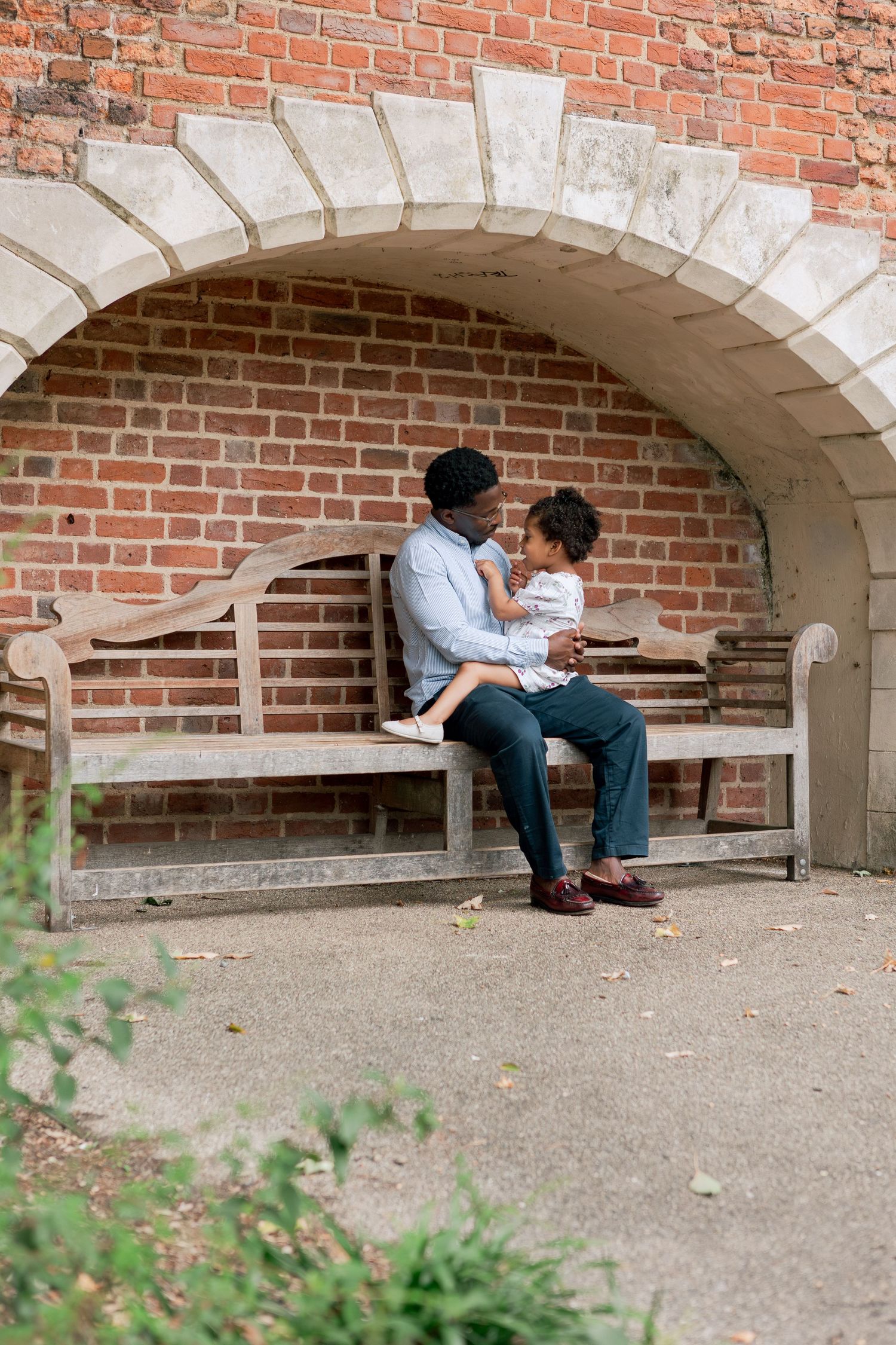 Toddler girl sitting on her father's lap on a park bench