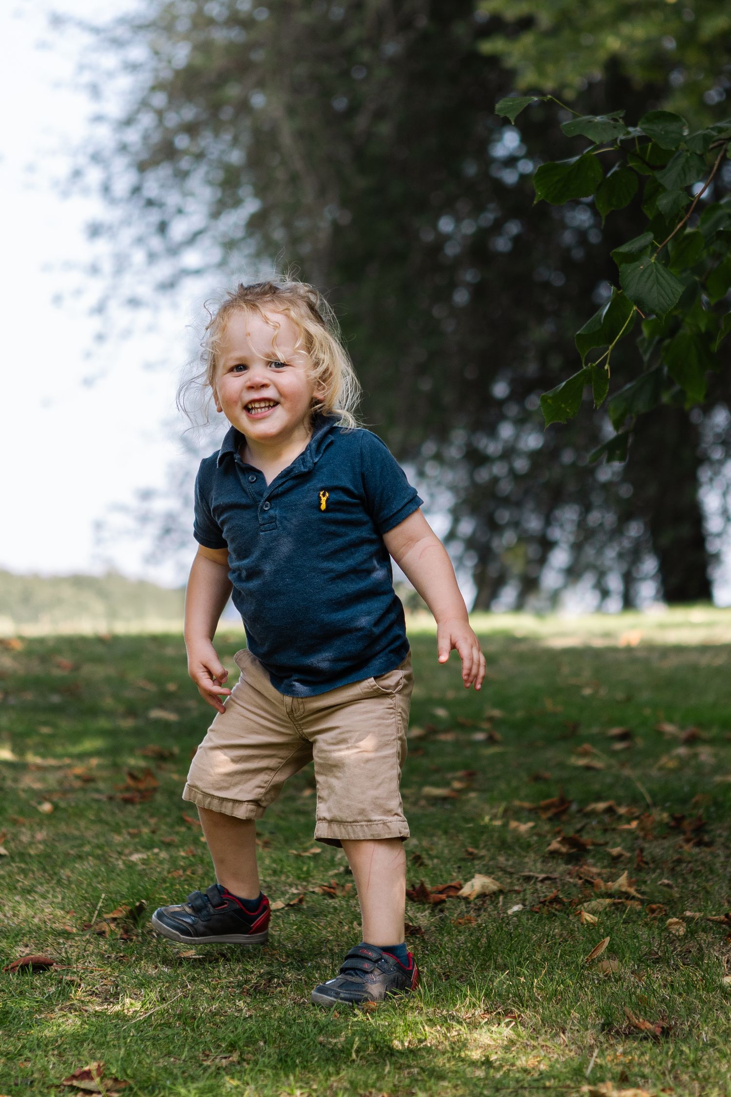 Toddler in park about to run away, looks towards camera and gives a big smile