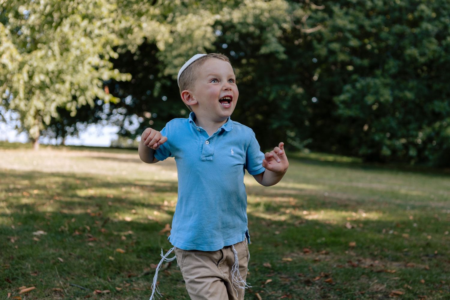 Boy laughs looking up at and chasing bubbles in park