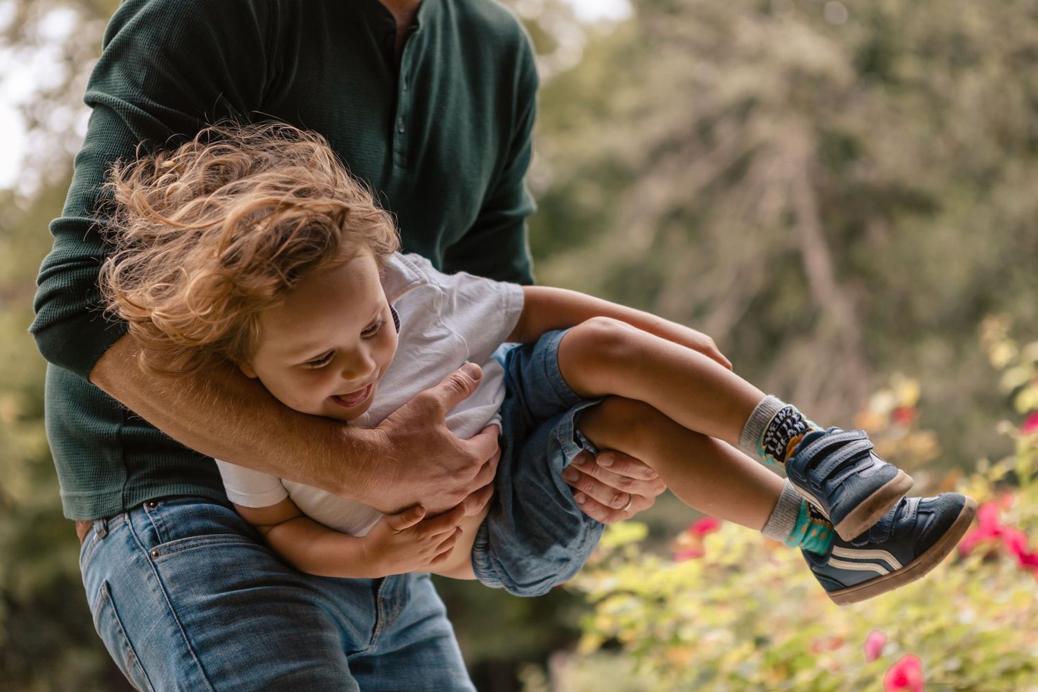 Father cradling and carrying toddler in the park, focus on toddler being carried