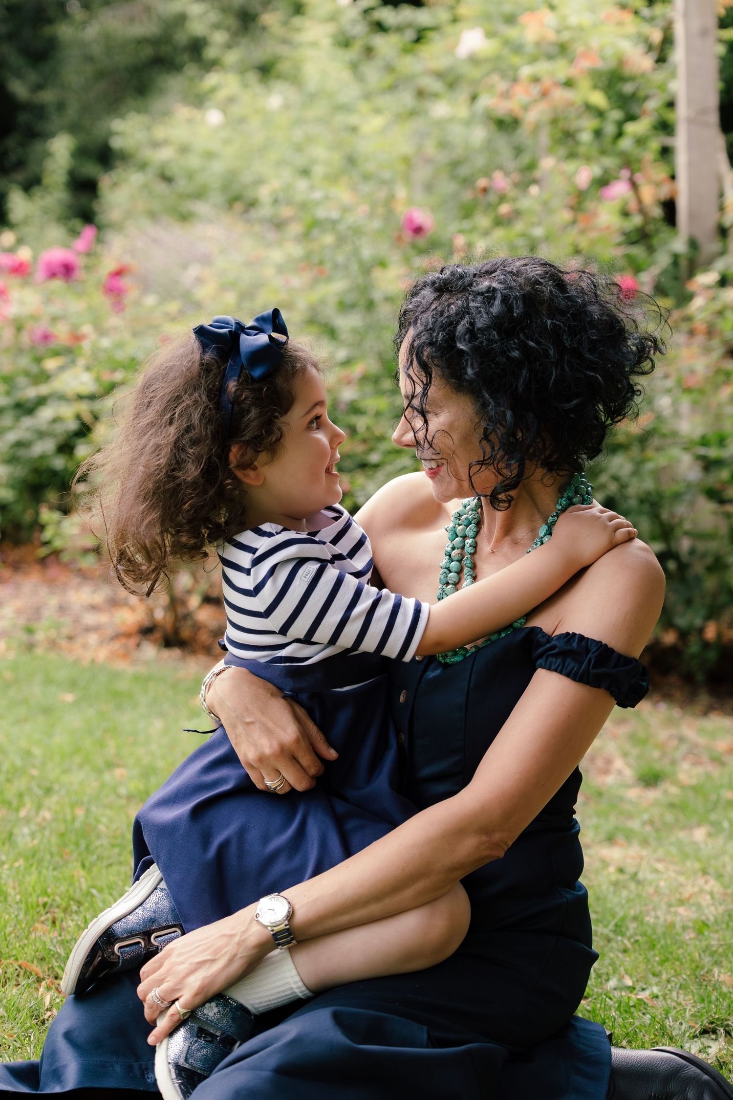 Mother sitting in park holding daughter on her lap, looking at each other smiling