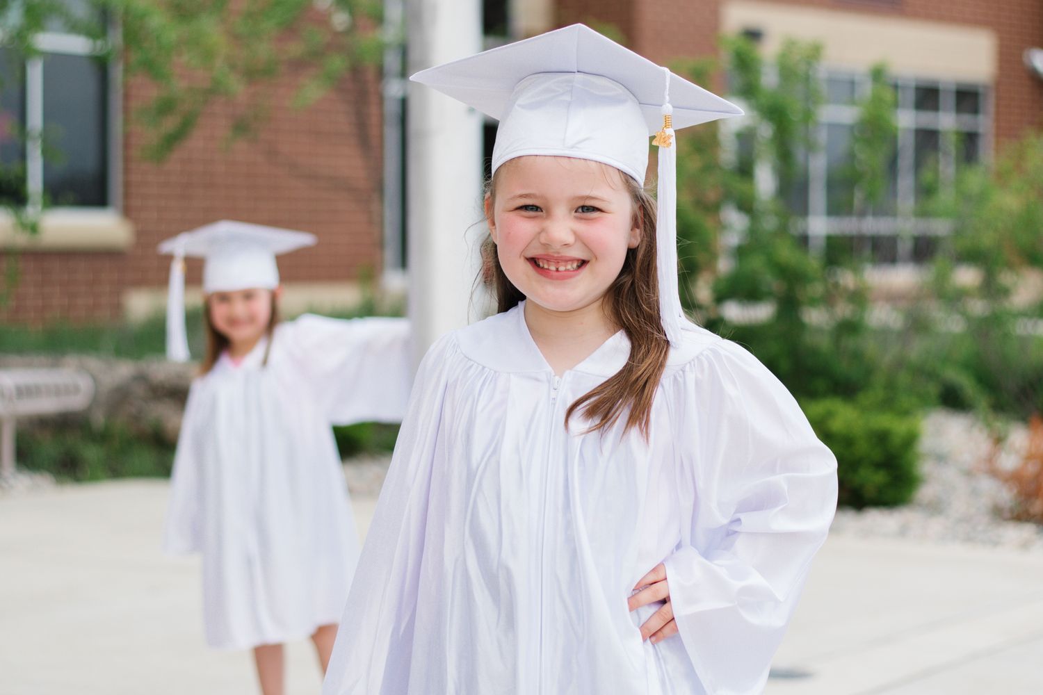 Graduate in white cap and gown smiles while standing outdoors.