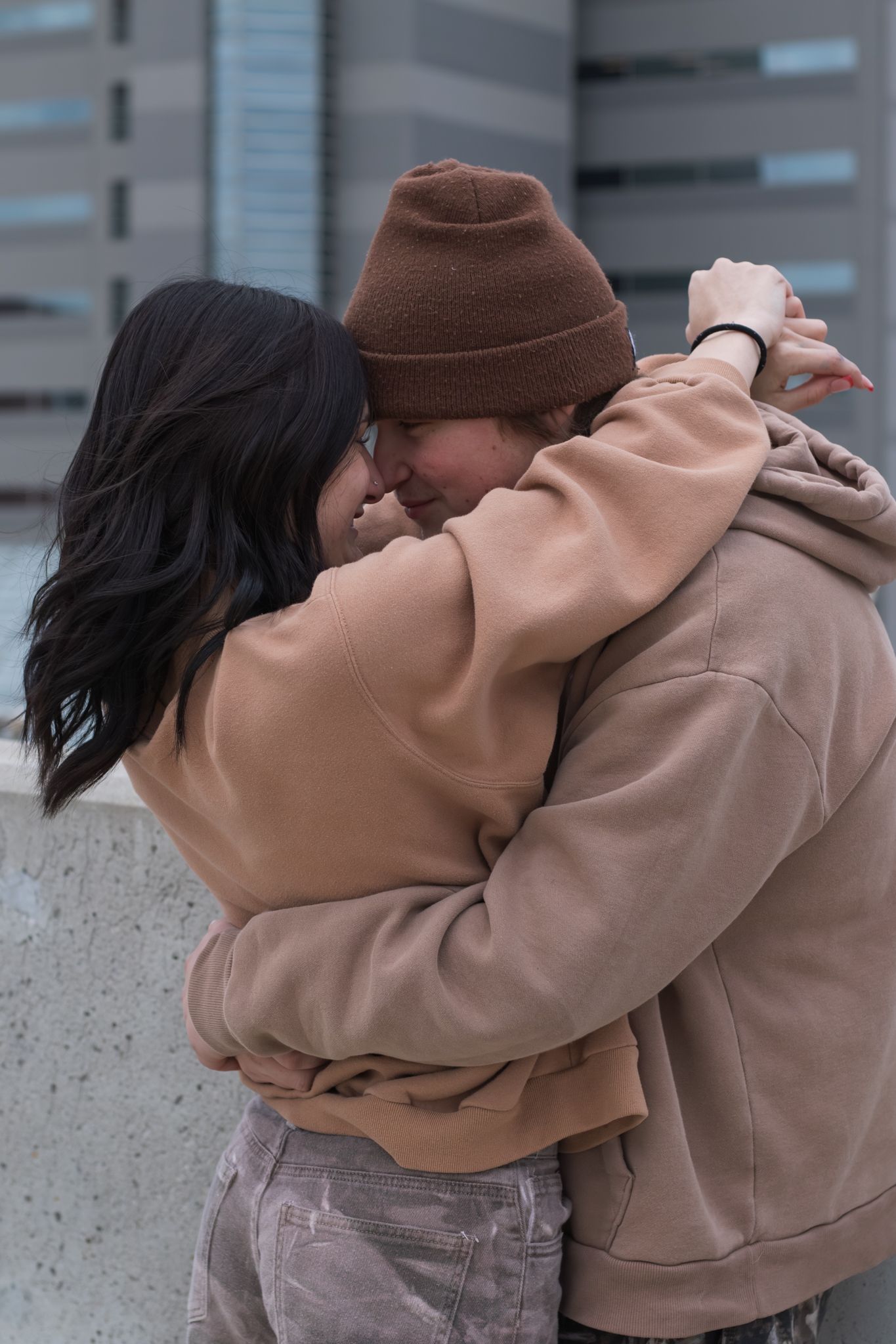 Couple in coordinating casual wear embrace intimately on a city rooftop.