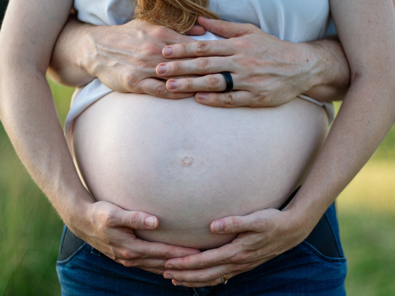 Gentle hands cradling a pregnant belly in afternoon sunlight.