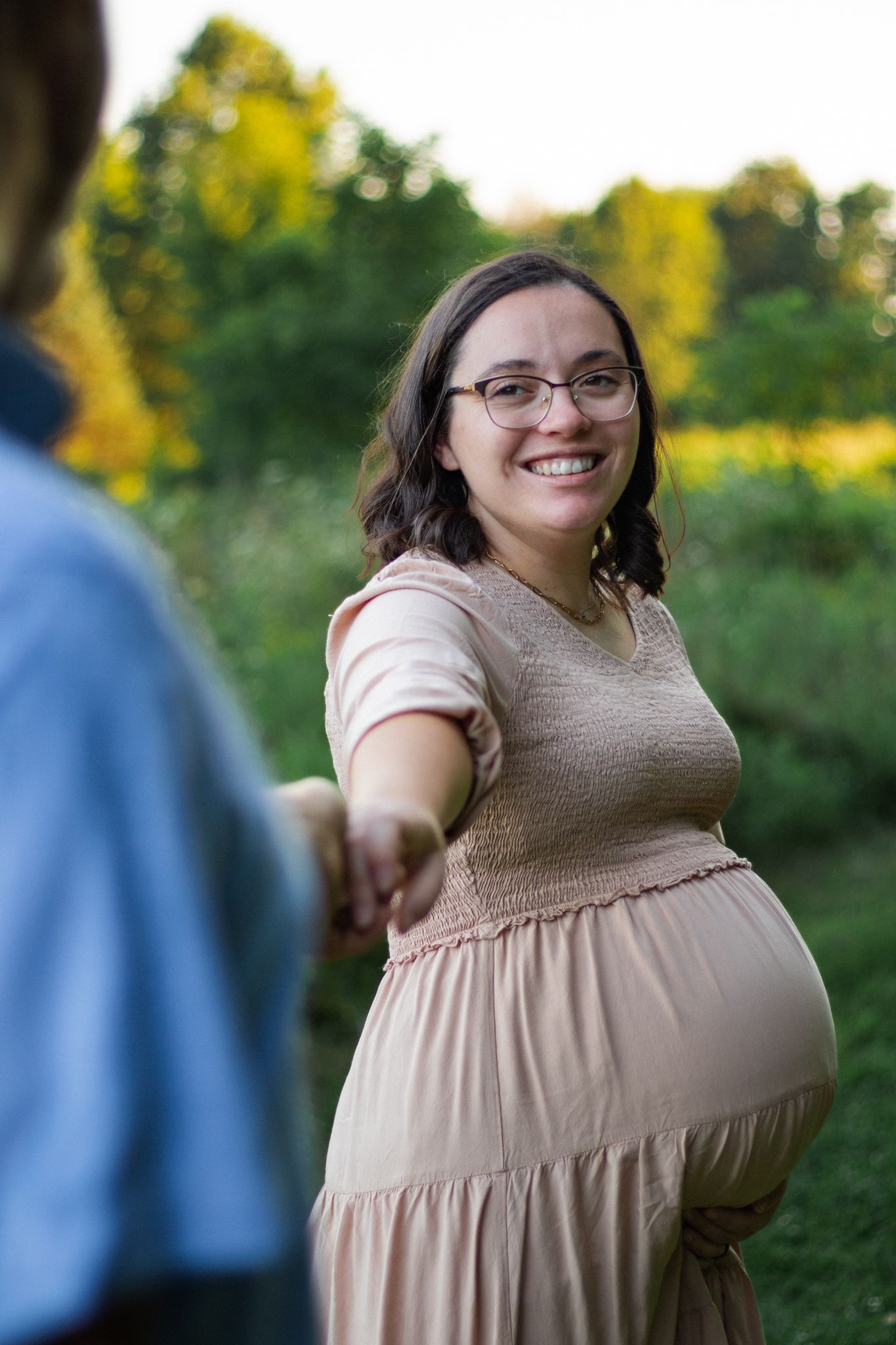 Joyful maternity portraits captured in a natural outdoor setting at sunset.