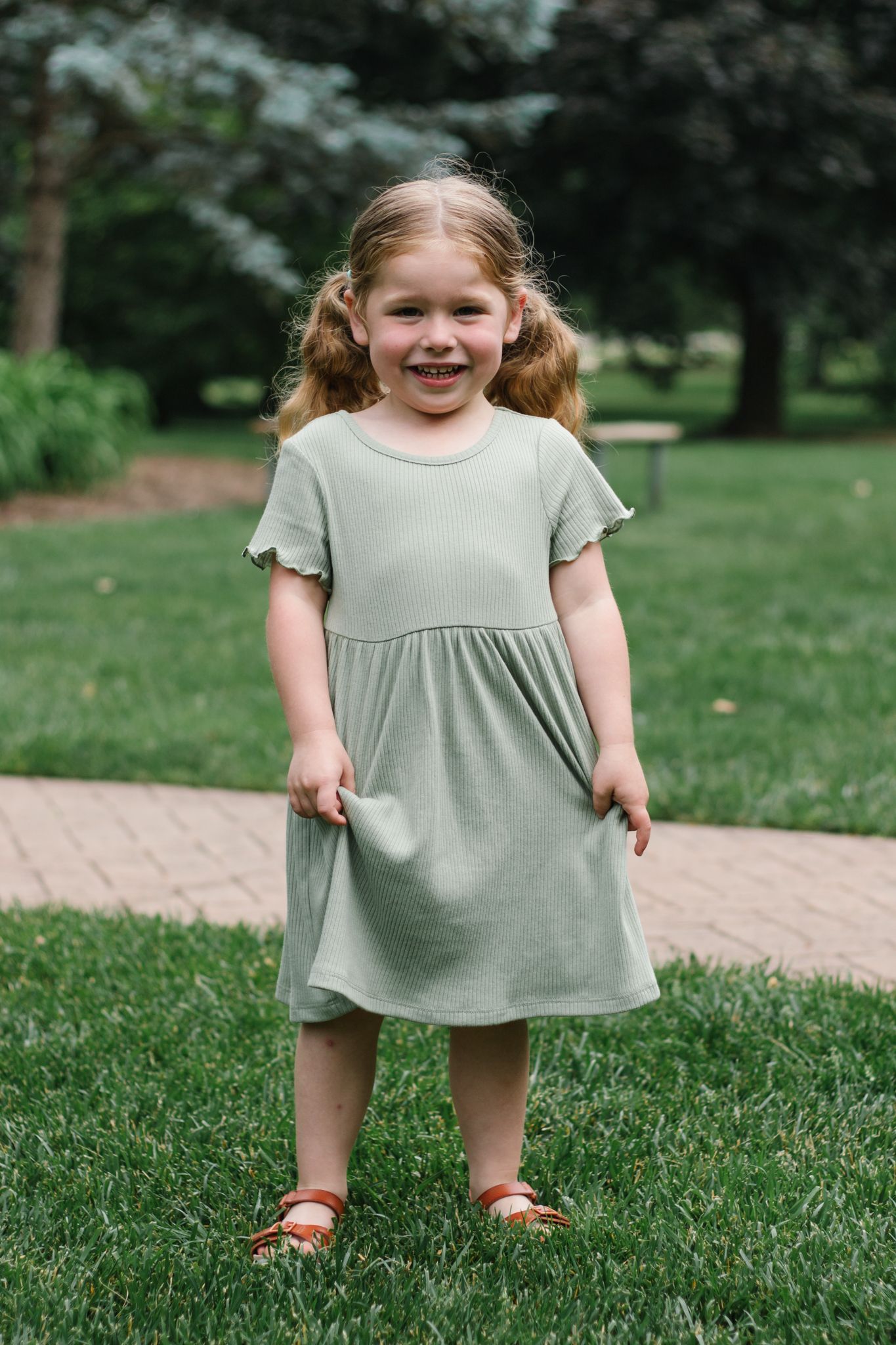 Child in light grey dress twirling and playing in a garden setting.